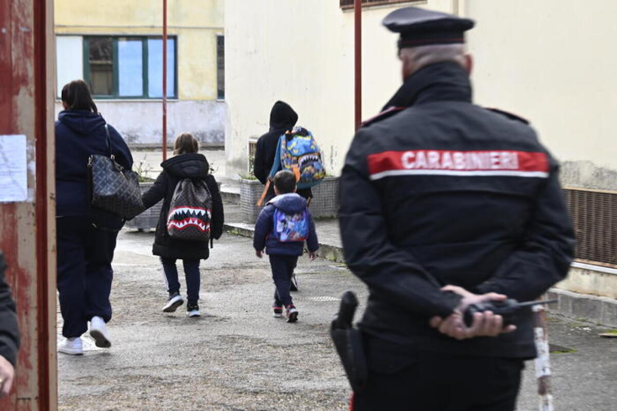 Arrestata una prof accusata di tenere comportamenti sessuali con minori - Bambini con gli zaini vanno verso la scuola media di Scanzano mentre un carabiniere li segue con lo sguardo, a Castellammare di Stabia, 18 novembre 2024. I militari presidiano l'istituto per prevenire tensioni in occasione della ripresa delle lezioni